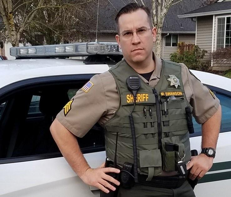 Matt Swanson, wearing a protective vest beside a patrol vehicle.